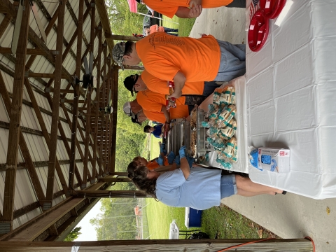 Assembly line serving food to a group of men in orange shirts