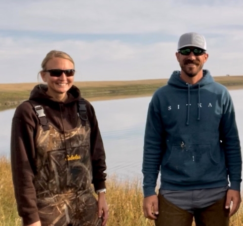 two people smiling and standing in front of a wetland
