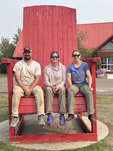 three people sit in a giant red chair