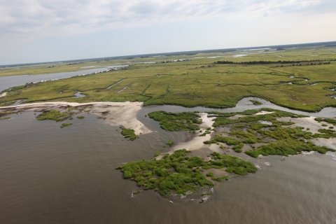 A coastal marsh taken by drone photography shows severe flooding throughout. Small sections of sand peak through the water where beaches once stood. 