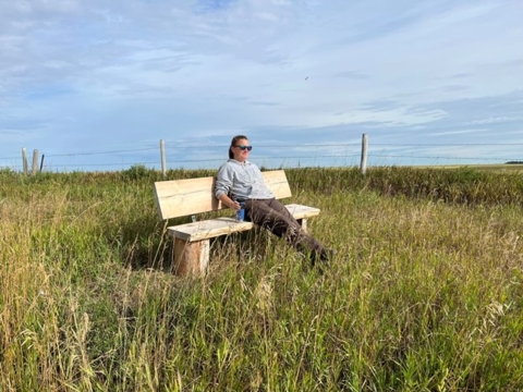 person sitting on a bench surrounded by grass and vegetations