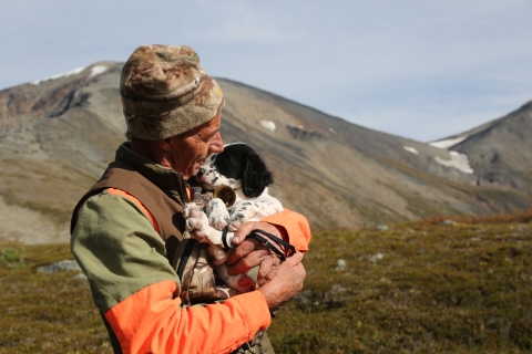 Hunter Steve Meyer carries a small puppy in his arms with treeless hills in the background. 