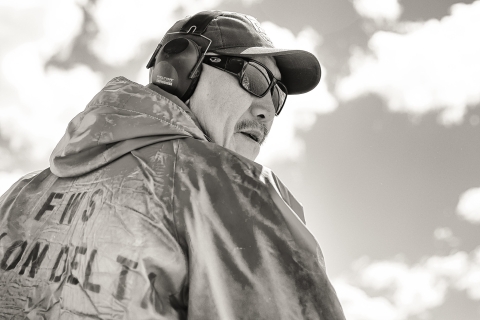 Non-color close up image of Chris Tulik wearing ear protection and sunglasses as he operates a watercraft on the Yukon River. 