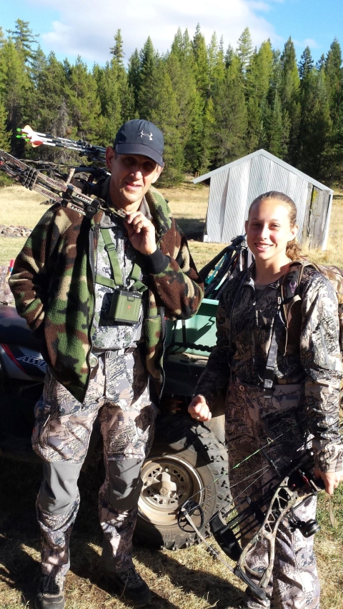 Hunter Emmett Walker and his daughter holding hunting equipment and standing in a field with trees behind them.