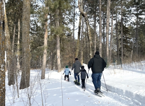 Adults and kids snowshoeing through the woods