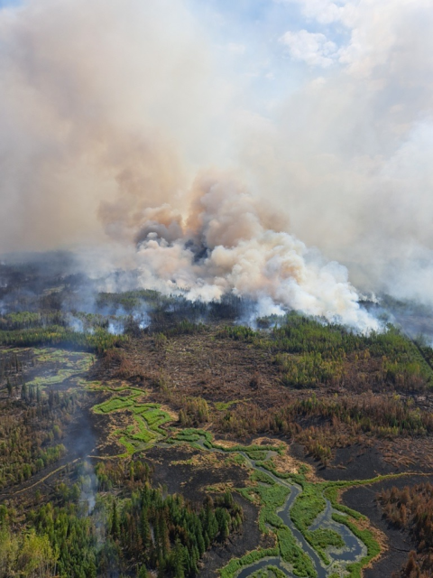 An aerial view of a fire on the landscape in Canada. The landscape is forested and there is a river running through the middle of the photo.