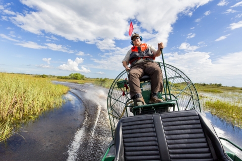 A man in a USFWS uniform rides through a swamp on a high-seated water vehicle. 