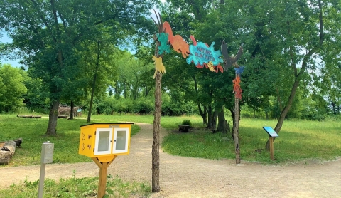 Nature play area welcome arch featuring art depictions of wildlif adjacent to a little free library.