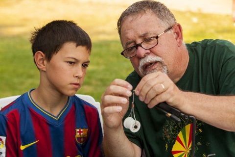 A man shows a boy seated next to him how to make a device, maybe for fishing.