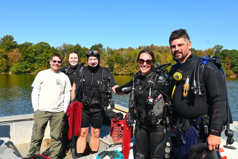 5 staff members on a boat in the Tennessee River. 4 of the staff members are wearing dive gear.