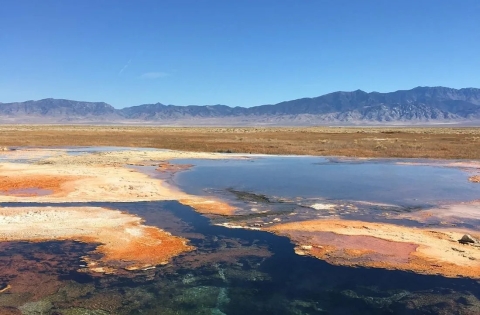 A hot spring is pictured with mountains in the background.