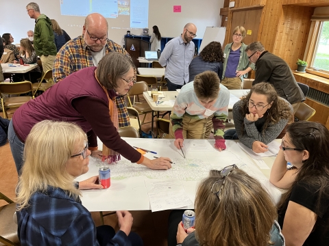 Several people sit and stand around a table looking at a map of the Connecticut River watershed