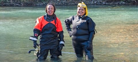 Two Service interns standing in a river wearing dry suits and snorkel gear.