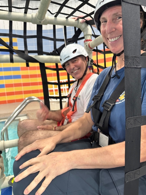 2 people strapped into pvc/harness cage; both wear helmets