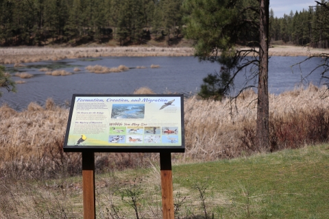 An interpretive wayside panel stands next to a lake