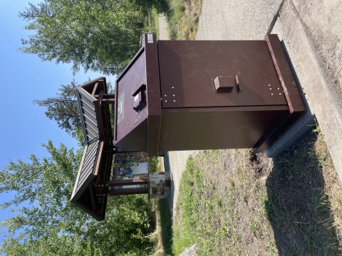 A brown trash can in front of an informational kiosk