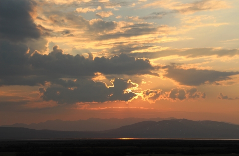 A hazy red-orange sunrise over a lake with mountain background.