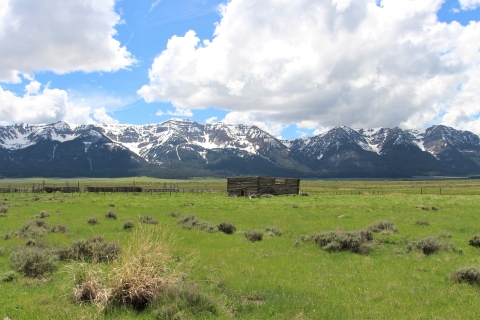 An abandoned collapsed wood building in a green valley with mountains in the background.