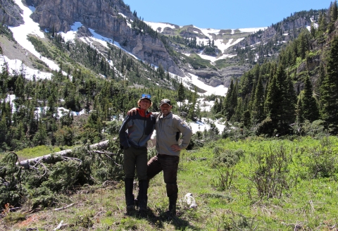 Two young men stand together for a picture with a snow covered mountain in the background.