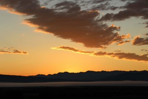 A red-orange early sunrise over a foggy middleground and mountainous background.