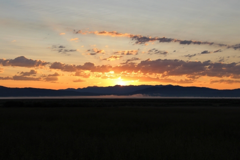 A red-orange early sunrise with sunrays over a foggy middleground and mountainous background.