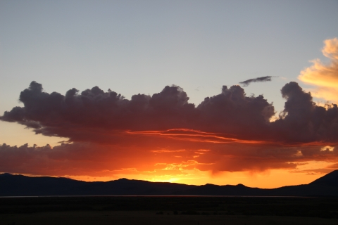 A red sunrise with dark clouds reflecting red light in a mountain background.