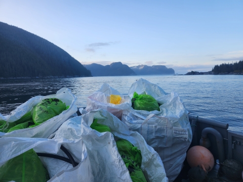 Trash bags piled on deck of boat with mountains highlighted by evening light in background.