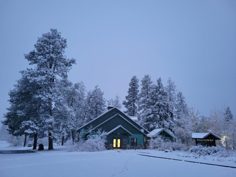 Snow blankets the trees and headquarters building of Turnbull NWR. A faint light can be seen from the glass front doors of the building.