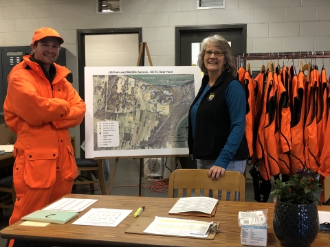 Lowell Haagenson and Lori Bennett inside the NCTC deer check-station surrounded by hunting area maps and blaze orange vests for hunters. 