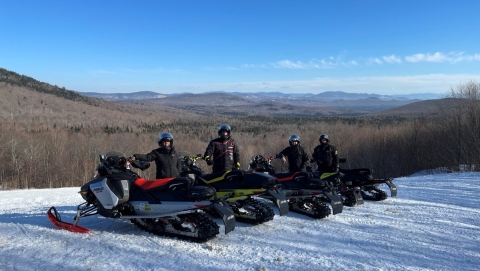 People on snowmobiles post on a trail that overlooks the mountains in Vermont