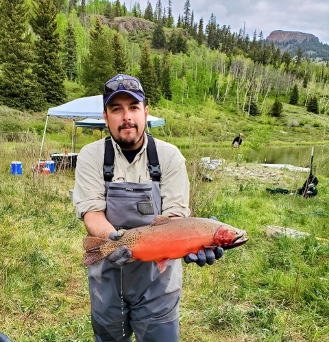 person stands and holds big trout parallel to ground
