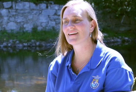 A white woman with long blonde hair and blue eyes wearing a blue polo shirt with a U.S. Fish and Wildlife Service logo