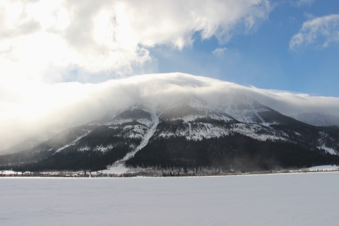 A wintery scene with clouds shrouding a snowy landscape and mountain.