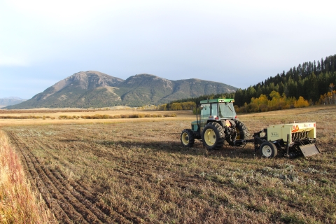 A parked tractor and seed drill is shown in a field with a mountain background.