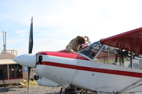 FWO Cody Smith with a fuel hose putting fuel into the wing tanks of a Top Cub bush plane with a remote fuel station in the background.