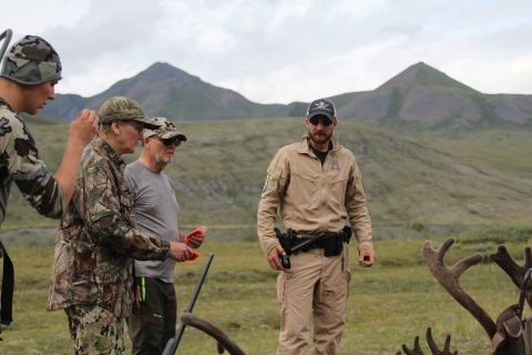 A Federal Wildlife Officer stands with three hunters as they get their licenses out with caribou antlers at the bottom of the image.