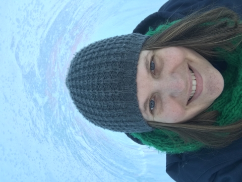 a person with long hair smiles and wears a hat and scarf