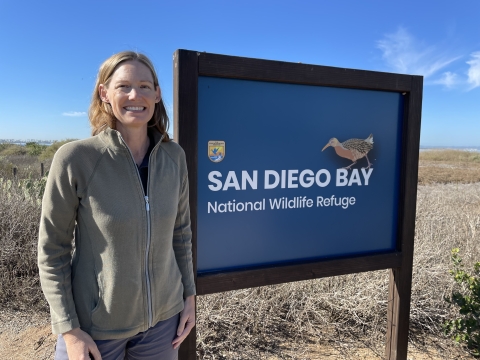 Woman standing next to a blue sign for San Diego Bay National Wildlife Refuge. 