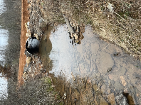 An old metal culvert covered by a dirt road. The culvert is degrading and threatens the road infrastructure.