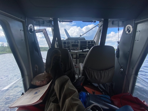 A POV image of the inside cabin of a float plane on the Gulkana River. The photographer's legs are comfortably crossed, and blue views of the river stream in through the plane's windows. 