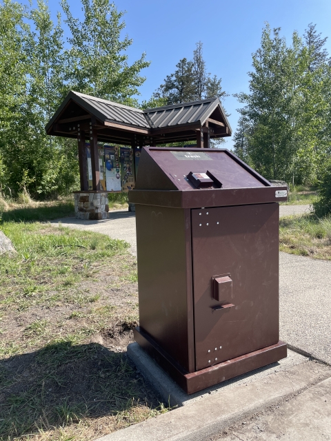 A brown trash can in front of an informational kiosk