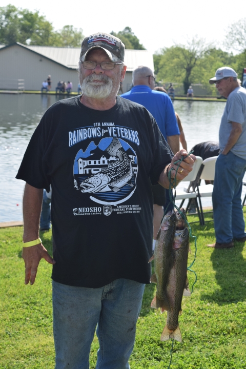 Man standing by the pond holding the four rainbow trout that he caught.