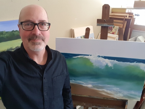 Artist Alan Bull in front of a painting of a wave