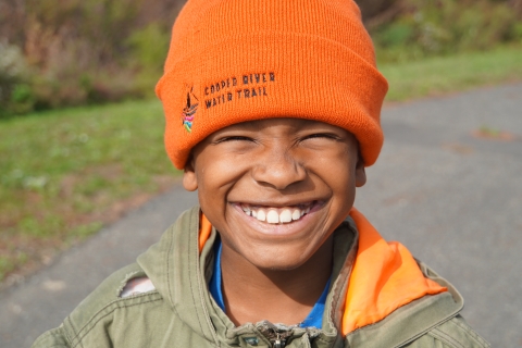 Boy wearing a "Cooper River Water Trail" winter hat, smiles broadly