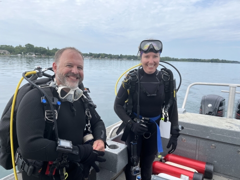 Two biologists in scuba gear smile aboard a boat on the Niagara River. 