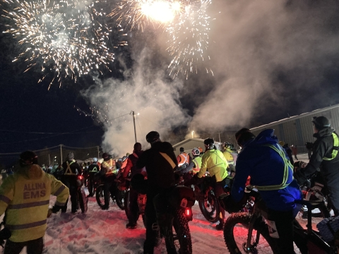 Fireworks fill the dark sky as racers set off on bike and on foot in an ultramarathon in Minnesota in winter.