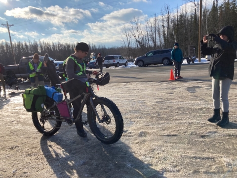 A man in a neon green harness stands in the cold alongside his fat-tire bike.