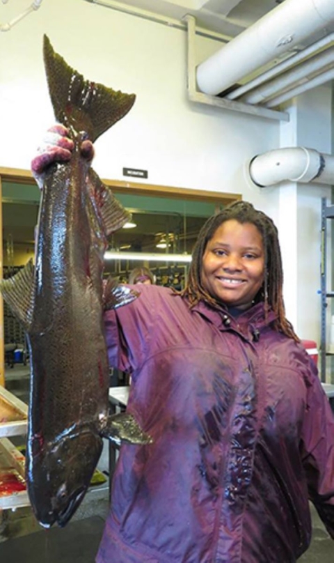 A woman smiles while holding up a very big fish by its tail.