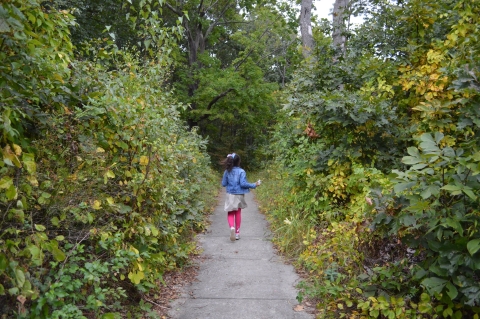 a young girl run down a sidewalk surrounded by dense forest foliage