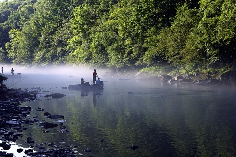 Children sitting on a rock fishing in a river with low-lying fog